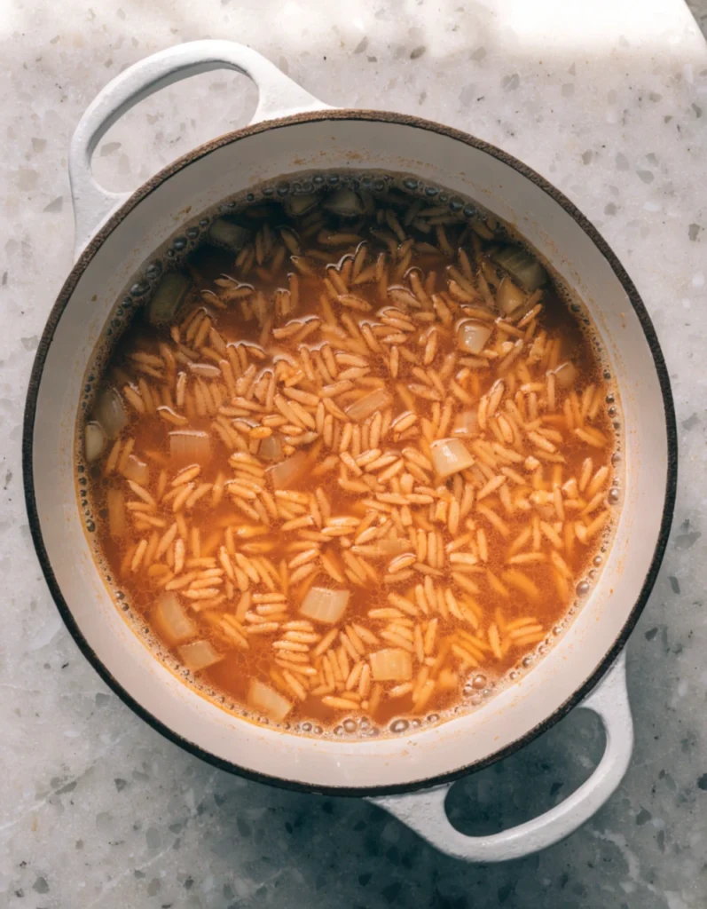 Tomato rice mixture boiling in chicken broth in skillet