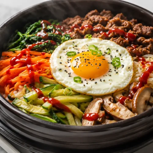 Korean bibimbap recipe in stone bowl with colorful vegetables, fried egg, beef, and gochujang sauce