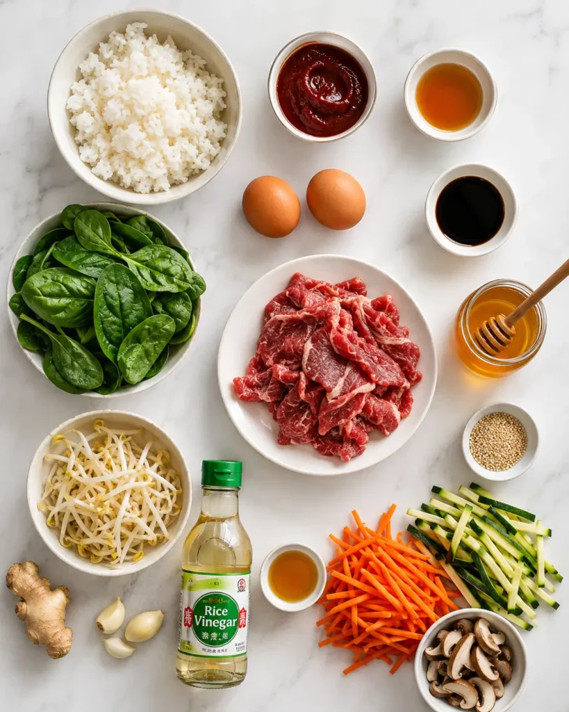 Bibimbap recipe ingredients arranged on marble surface including rice, vegetables, beef, gochujang, and sesame oil